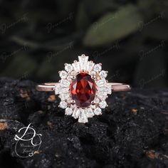 a ring with a large red stone surrounded by small white diamonds on top of a rock