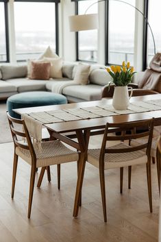 a living room filled with furniture and a table in front of large windows on top of a hard wood floor