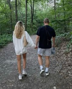 a man and woman walking down a path in the woods holding hands with each other