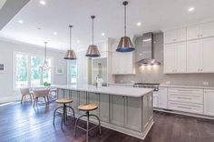 a large kitchen with white cabinets and wood flooring is pictured in this image, there are two stools at the center of the island