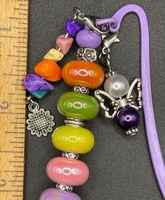 an assortment of colorful beads and charms on a table next to a measuring ruler with a purple handle