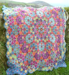 a multicolored crocheted quilt on the grass