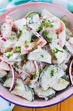 a pink bowl filled with cucumber salad on top of a blue and white towel