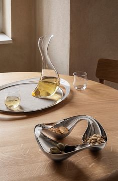 two wine glasses sitting on top of a wooden table next to a silver tray with olives