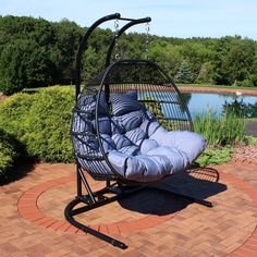 a swing chair sitting on top of a brick patio next to a body of water