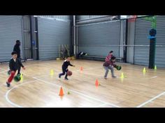 children playing basketball on an indoor court surrounded by orange and green cones with people watching