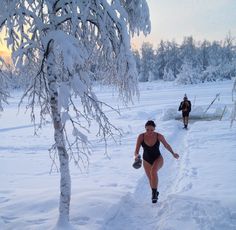 a woman in a black swimsuit is walking through the snow with two other people behind her