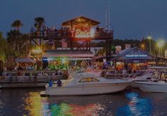 two boats are docked in the water at night near a pier with people on it