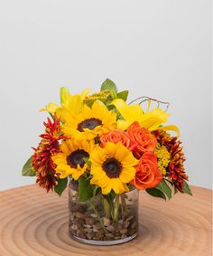 an arrangement of sunflowers, roses and other flowers in a glass vase on a wooden table