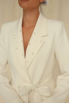 a woman in a white suit with a bow around her waist and hands on her hips