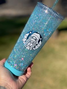 a hand holding up a blue starbucks cup with glitter on it's lid and straw