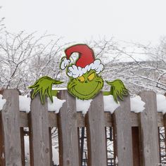 a wooden fence with a grin face painted on it's side and snow covered trees in the background