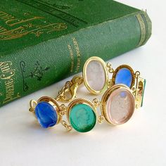 A stunning collection of Venetian glass cameo/intaglios in lapis blue, emerald green and blush pink, have been married together to create this classic bracelet. Each of the gorgeous intaglios/cameos sits in bezeled mountings accented with a twisted border made of gold vermeil. This neoclassical design is simultaneously understated and dynamic with it’s simple classic designs and coloring. This jaw-dropping bracelet with roots in the Byzantine era, will quickly become a favorite due to its classi Elegant Glass Bracelet Jewelry, Formal Blue Bracelets With Cabochon, Elegant Glass Jewelry With Cabochon, Victorian Bracelets With Polished Finish, Luxury Gold Cameo Bracelet, Elegant Blue Glass Bracelets, Carnelian Cameo Jewelry Gift, Elegant Blue Glass Bracelet, Luxury Victorian Cameo Bracelet