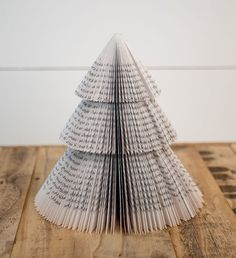 an origami christmas tree made out of book pages on a wooden table with white wall in the background