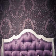 a purple and white bed in front of a wall with damasks on it