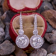 two diamond earrings sitting in a red velvet box on some rocks and gravel with stones around them