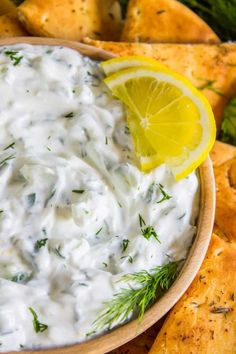 a wooden bowl filled with sour cream dip surrounded by crackers and lemon wedges