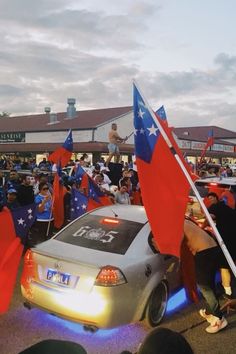 a crowd of people standing around a car with flags on it