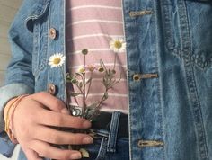 a person wearing a jean jacket with daisies in their pockets and holding onto a cell phone