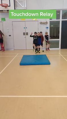 several children are standing on a blue mat in an indoor basketball court