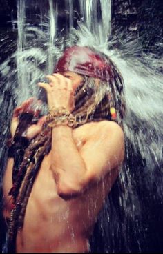 a man with dreadlocks standing under a waterfall