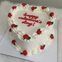 a white heart shaped cake with red roses on the top and writing happy valentine's day