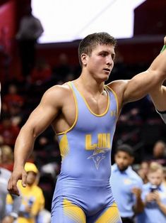 a wrestling player holding his fist up in the air with other wrestlers behind him and onlookers watching