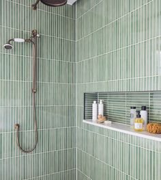 a green tiled bathroom with shower head and shelf