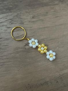 a pair of gold and white beaded flowers on a keychain that is sitting on a wooden table