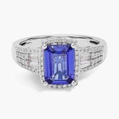 This ring showcases an emerald-cut tanzanite gemstone accented by baguette sidestones and framed with sparkling round diamonds in 14k white gold. Emerald Cut Sapphire Ring With Baguette Diamonds, Emerald Cut Tanzanite Diamond Ring, Luxury Tanzanite Diamond Ring With Emerald Cut, Tanzanite Gemstone Ring In Baguette Cut, Baguette Cut Tanzanite Ring With Prong Setting, Classic Tanzanite Emerald Cut Diamond Ring, Elegant Tanzanite Emerald-cut Diamond Ring, Elegant Tanzanite Emerald Cut Diamond Ring, Baguette Cut Tanzanite Jewelry With Accent Stones