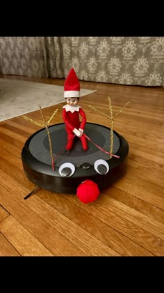 an elf is sitting on top of a robotic vacuum cleaner with eyes and nose painted red