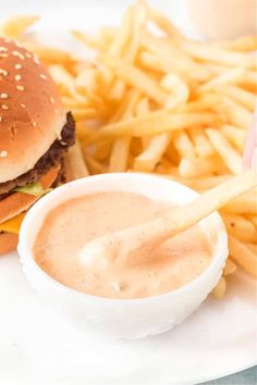 a hamburger and fries on a plate with dipping sauce in a small white bowl next to it