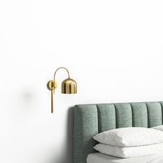 a bed with white pillows and a green headboard next to a gold wall light