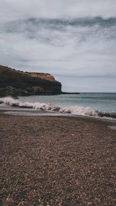 an empty beach with waves coming in to the shore and a rocky cliff on the other side