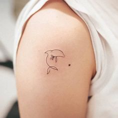 a small dolphin tattoo on the back of a woman's left arm, which is black and white