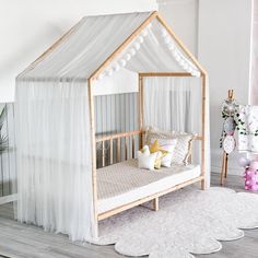 a white bed with sheer curtains and pillows on it's sides in a room