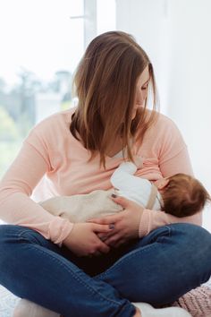 a woman holding a baby in her arms while sitting on the floor next to a window