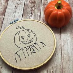 a pumpkin with a man's face drawn on it next to an embroidery hoop