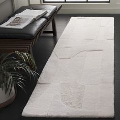 a large white rug in the middle of a room next to a bench and window