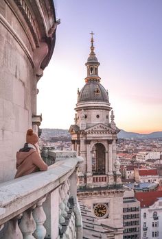 a teddy bear sitting on the ledge of a building with a view of buildings in the background