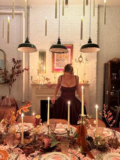 a woman standing in front of a table with plates and candles on top of it