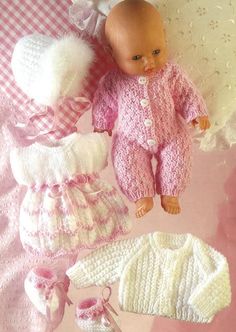 a baby doll laying on top of a blanket next to knitted clothes and booties