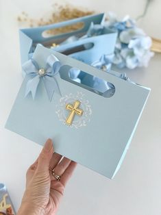 a person holding up a blue paper bag with a cross on it and flowers in the background