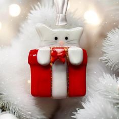 a red and white cat ornament hanging from the side of a christmas tree