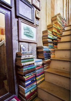 a bunch of books that are sitting on the stairs in front of a mirror and framed pictures