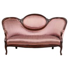 an old fashioned pink couch with wood trimmings on the arms and back, against a white background