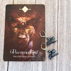 a pair of earrings sitting on top of a wooden table next to a card with an image of a panther