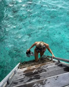 a woman standing on the edge of a boat looking down at water and corals