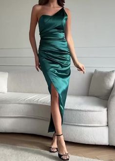 a woman in a green dress is standing near a white couch and looking at the camera