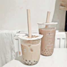 two iced coffee drinks sitting on top of a white table next to eachother